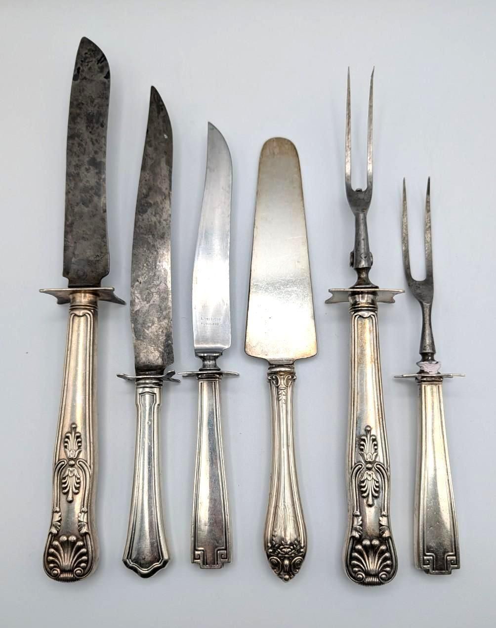 Six antique serving utensils with ornate silver handles arranged vertically against a plain white background.