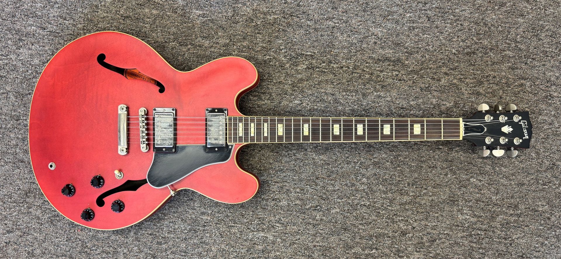 Red semi-hollow electric guitar lying on gray carpet