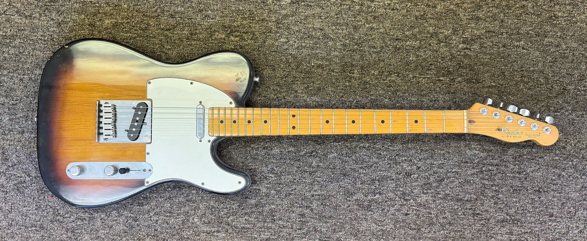 Sunburst electric guitar with white pickguard lying on gray carpet