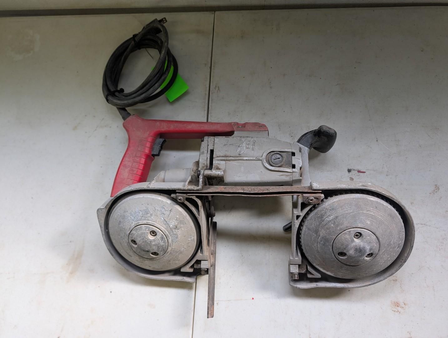 A red and gray portable band saw with a black power cord, resting on a white surface.