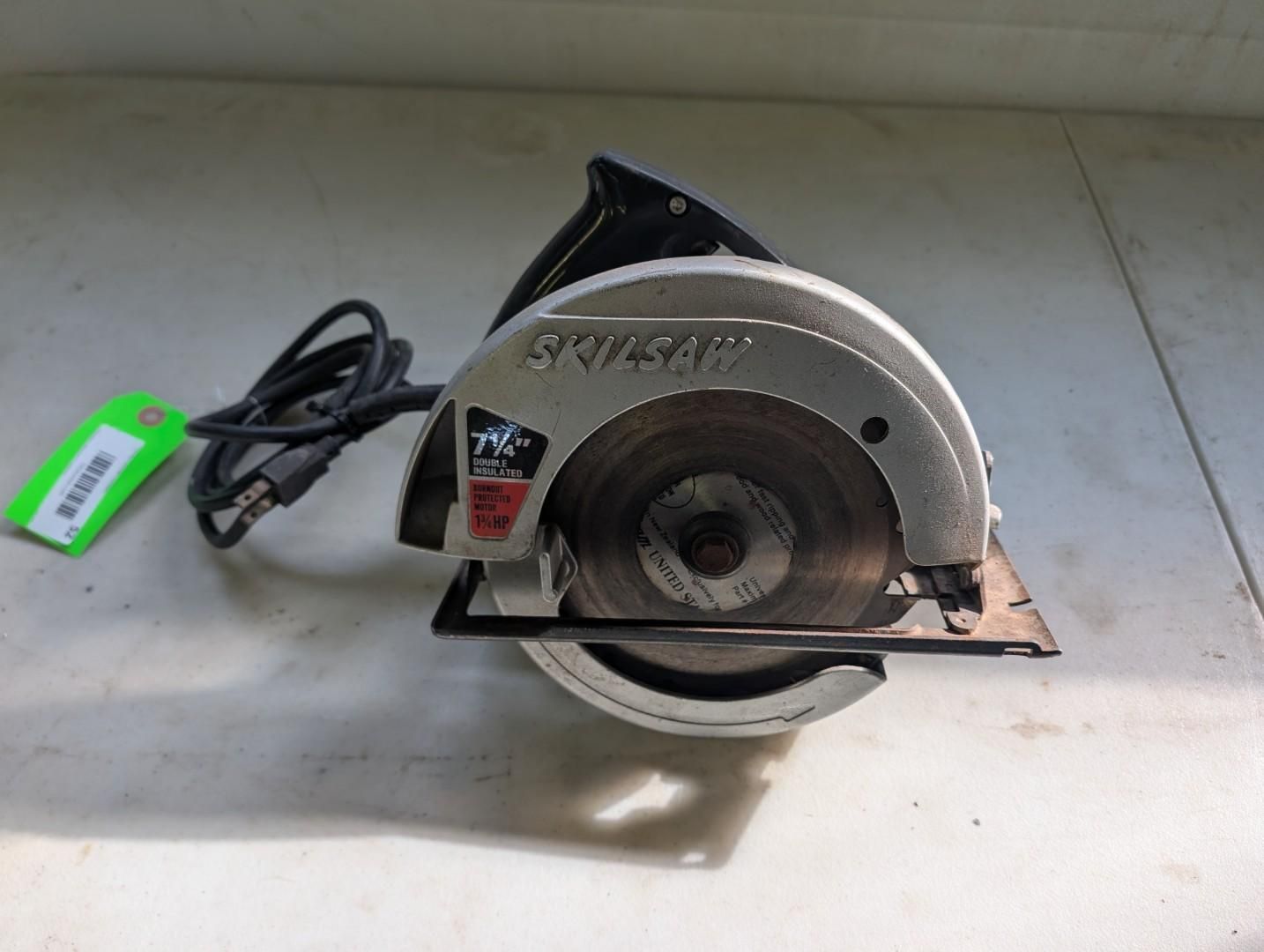 Circular saw on a white surface with a black cord and a green tag attached.