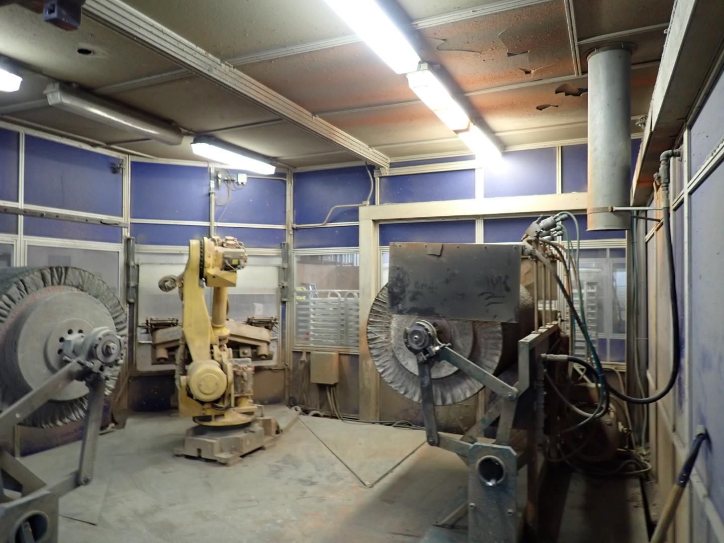 Yellow robot arm in an industrial workshop, surrounded by large grinding wheels and machinery.