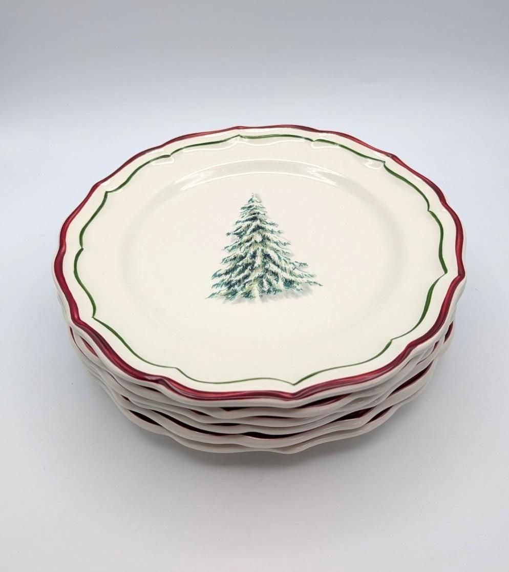A stack of off-white ceramic plates with scalloped edges, decorated with green and red rims and a centered pine tree.