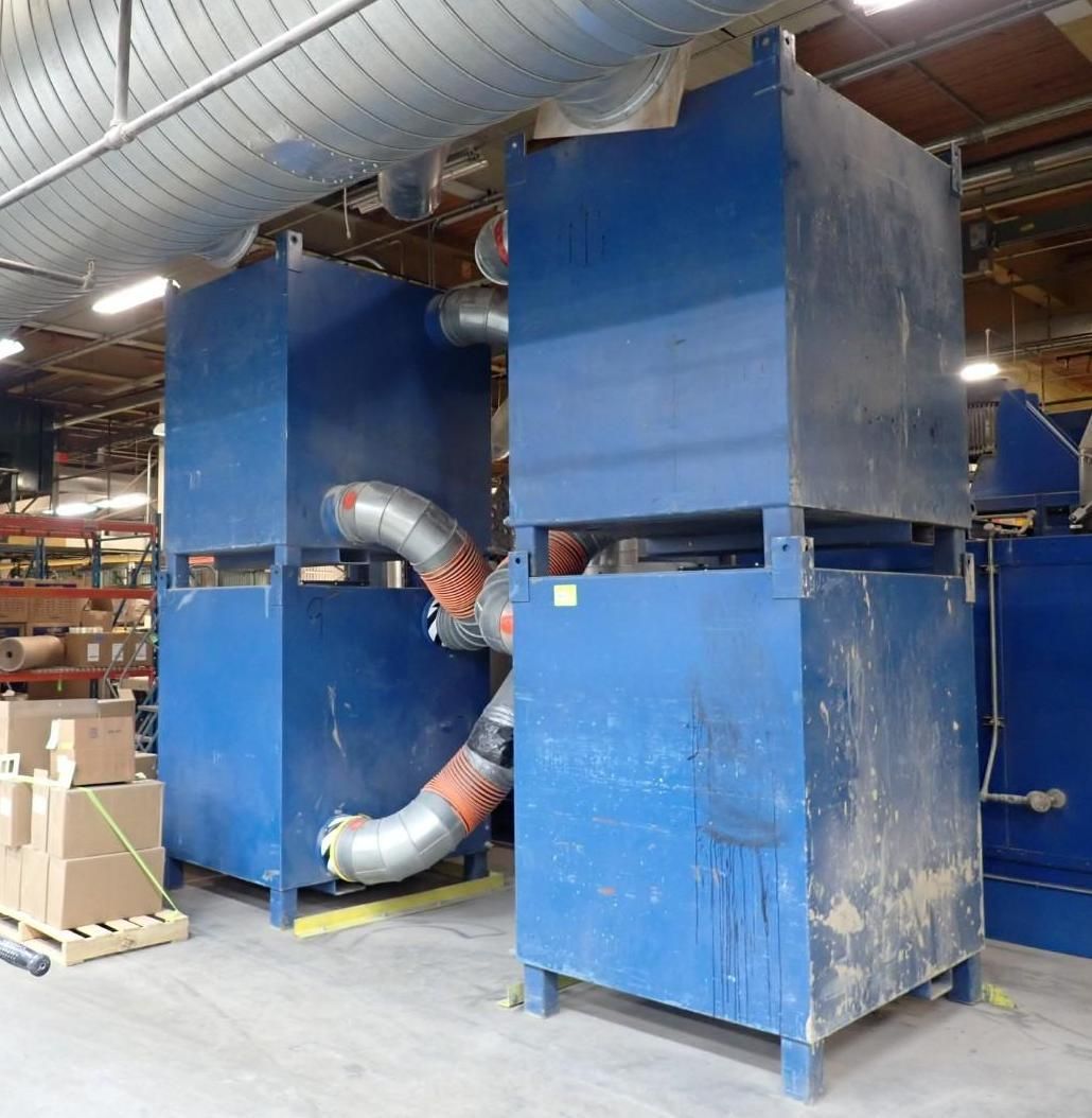 Two blue industrial dust collection units in a warehouse setting, connected by flexible ductwork.