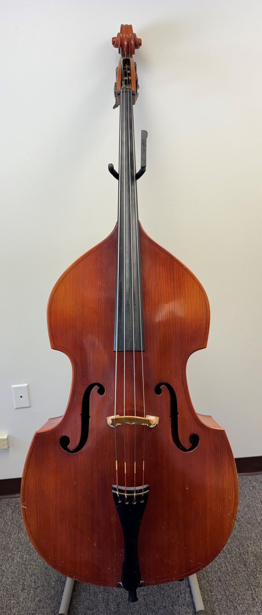 A wooden upright bass standing against a plain wall.