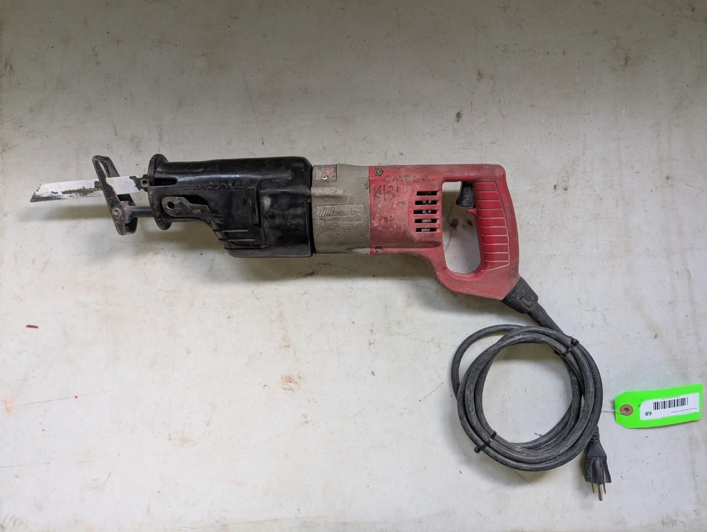 Red and black reciprocating saw with blade extended, lying on a white surface with a power cord and a green tag.