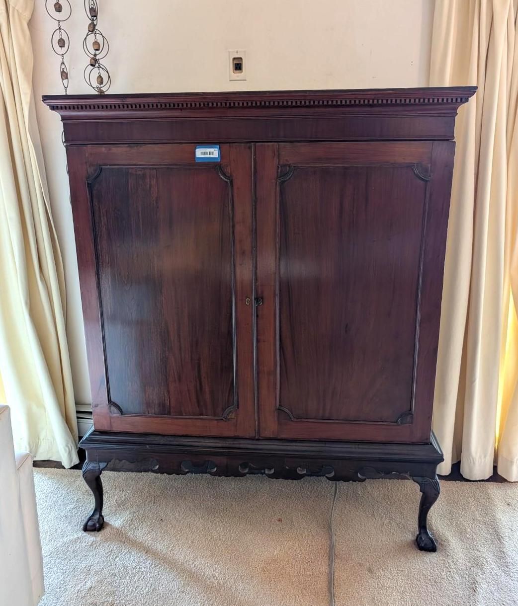 A tall, dark wood double-door cabinet featuring a decorative top molding, cabriole legs, and claw-and-ball feet.