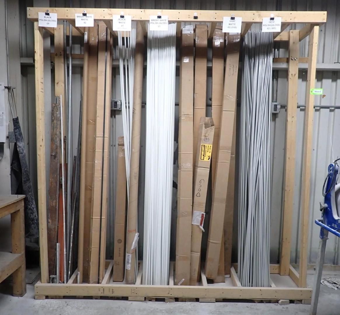 Wooden storage rack holding various lengths of building materials, including wrapped metal, wood, and other types.