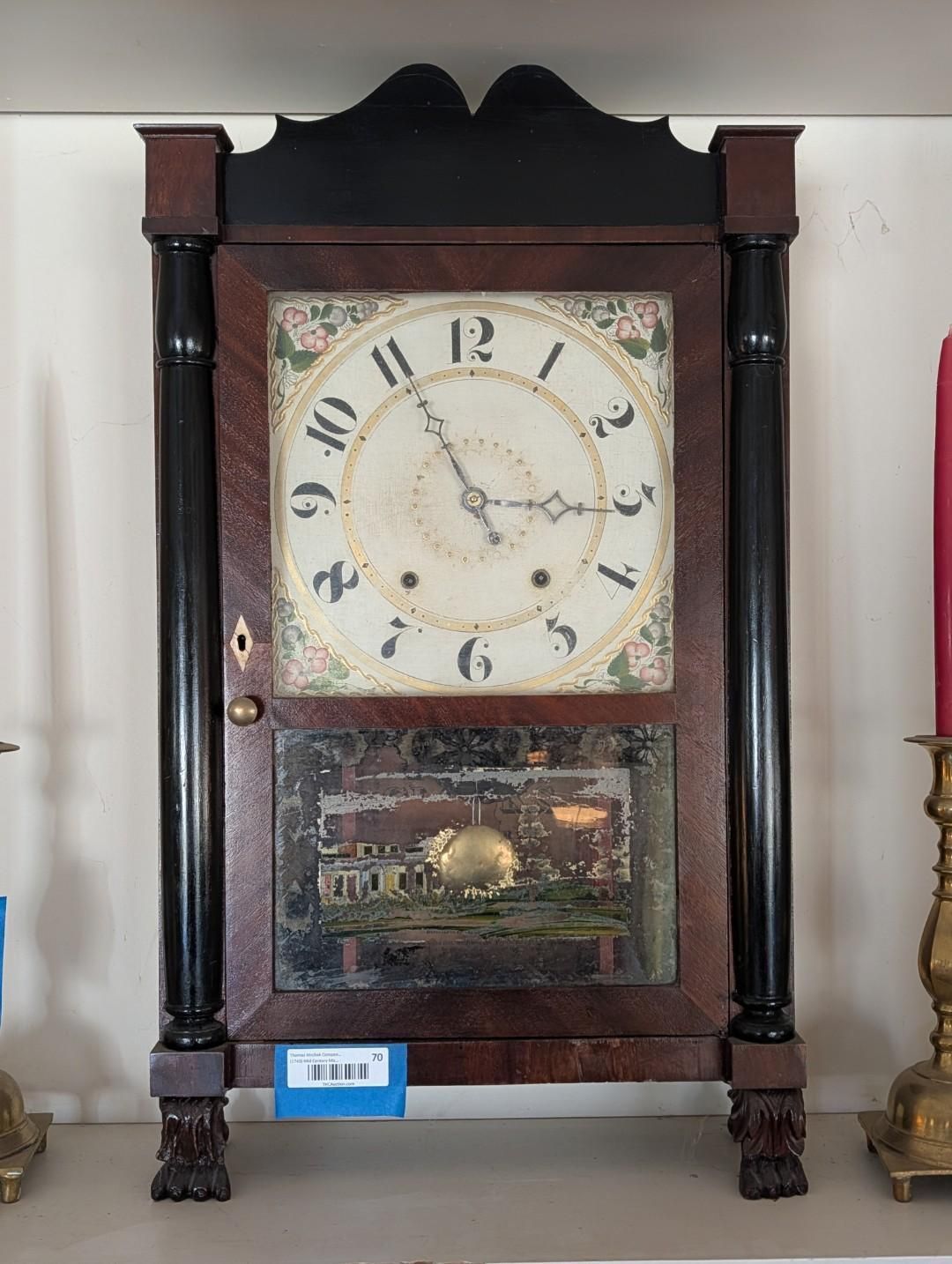 Antique wooden grandfather clock with cream face and decorative painted lower panel against a red wall