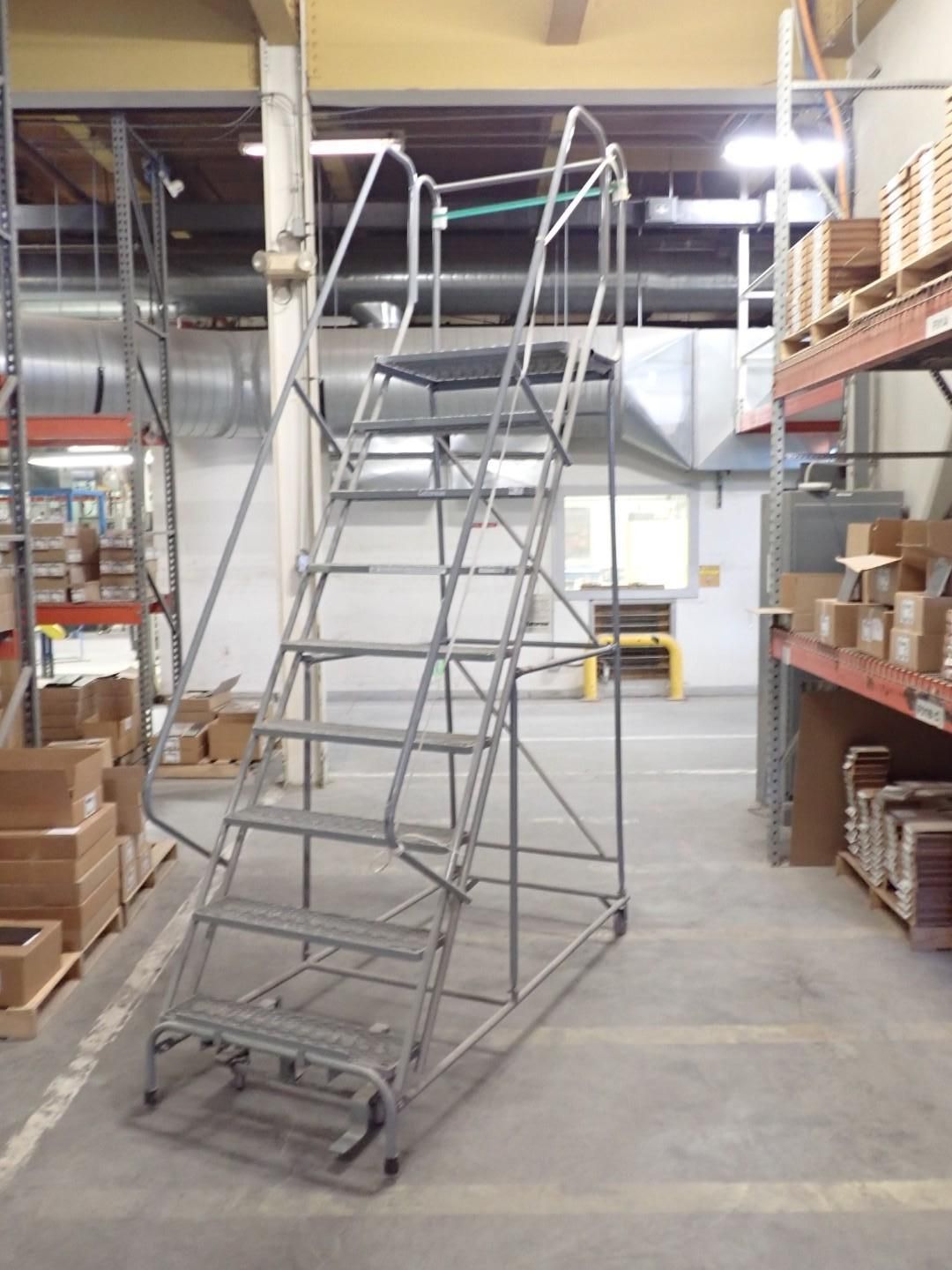 Gray rolling staircase in warehouse aisle, leading to a small platform.