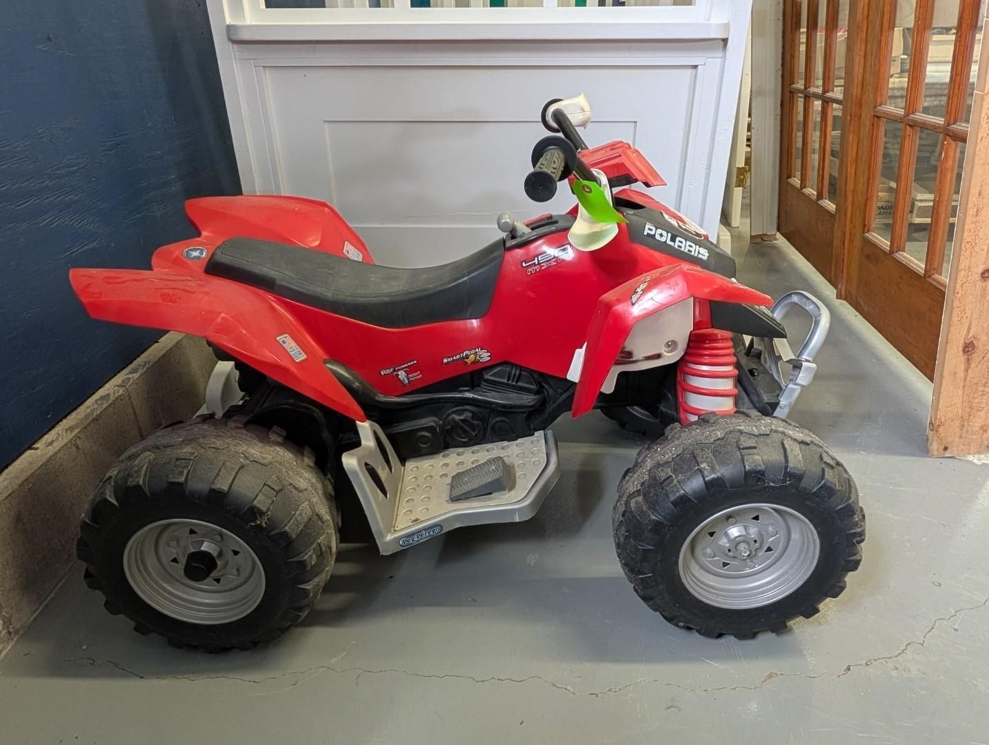 Red toy ATV with black seat and wheels, parked indoors.
