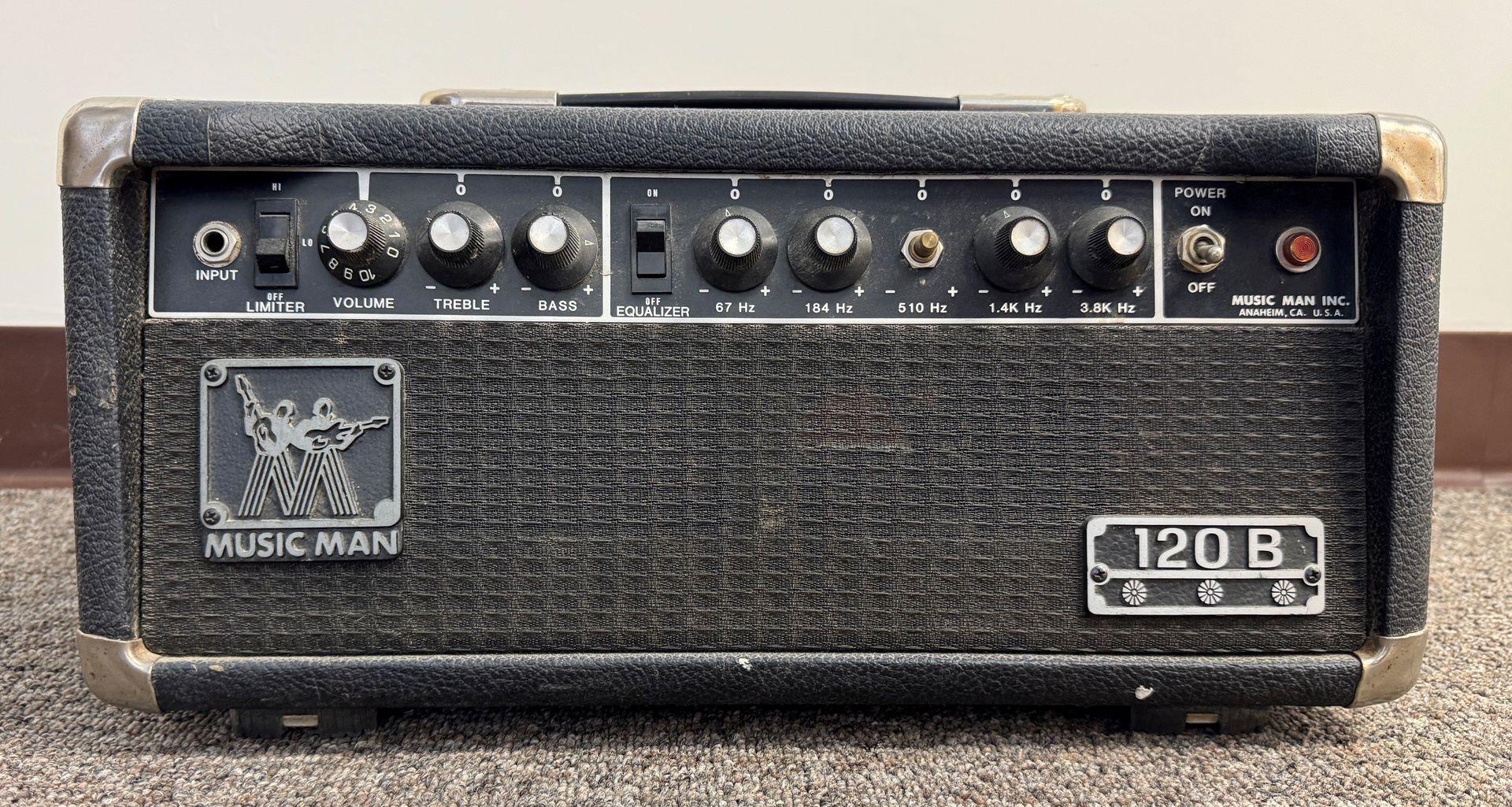 Black Music Man 120B guitar amplifier with control knobs and textured grille on a rough surface