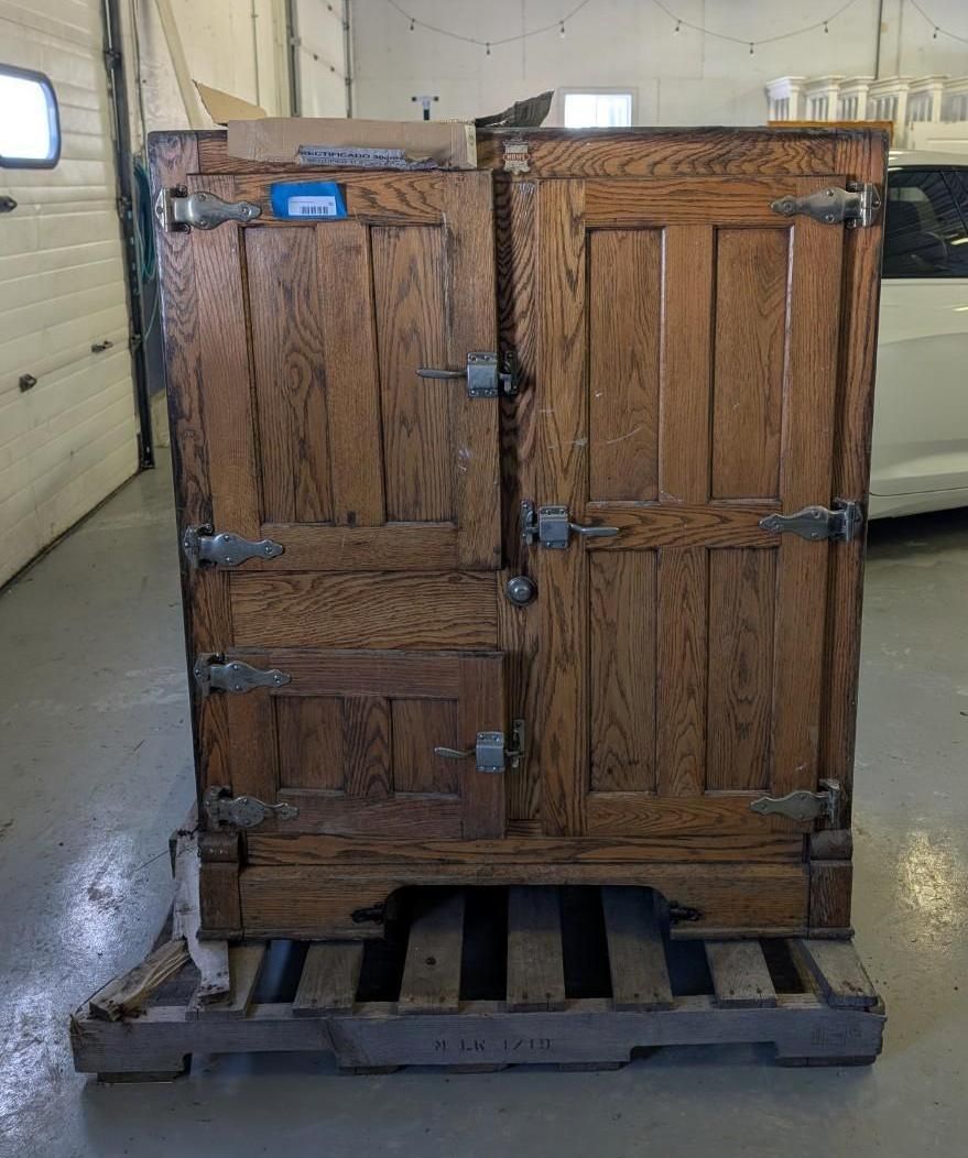 Antique wooden icebox on a pallet, two doors, metal latches, and hinges.