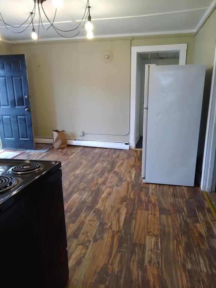 A kitchen view with wood-look flooring, a black stove in the foreground, a dark door, and a white refrigerator.