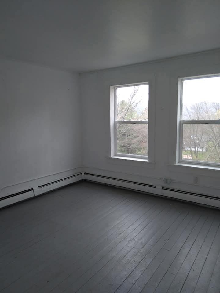 An empty room with white walls, two windows looking outside, and gray painted wood flooring.