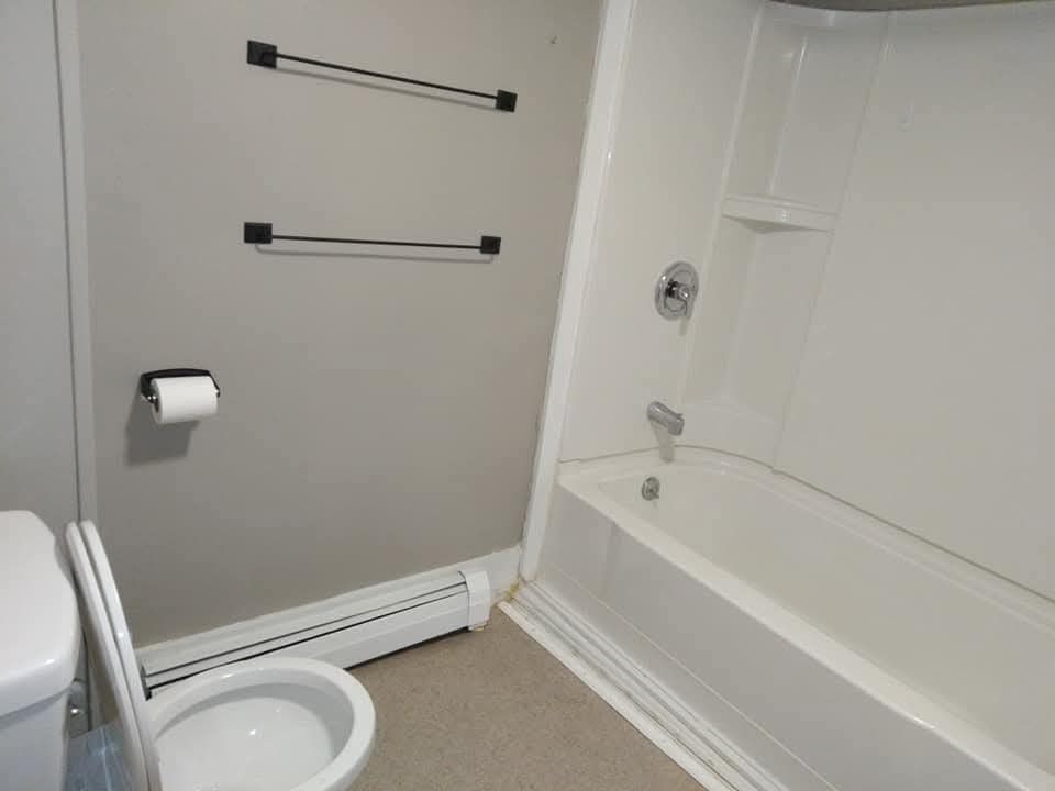 A bathroom with a white toilet, a white bathtub with a showerhead, a toilet paper holder, and two wall-mounted towel bars.