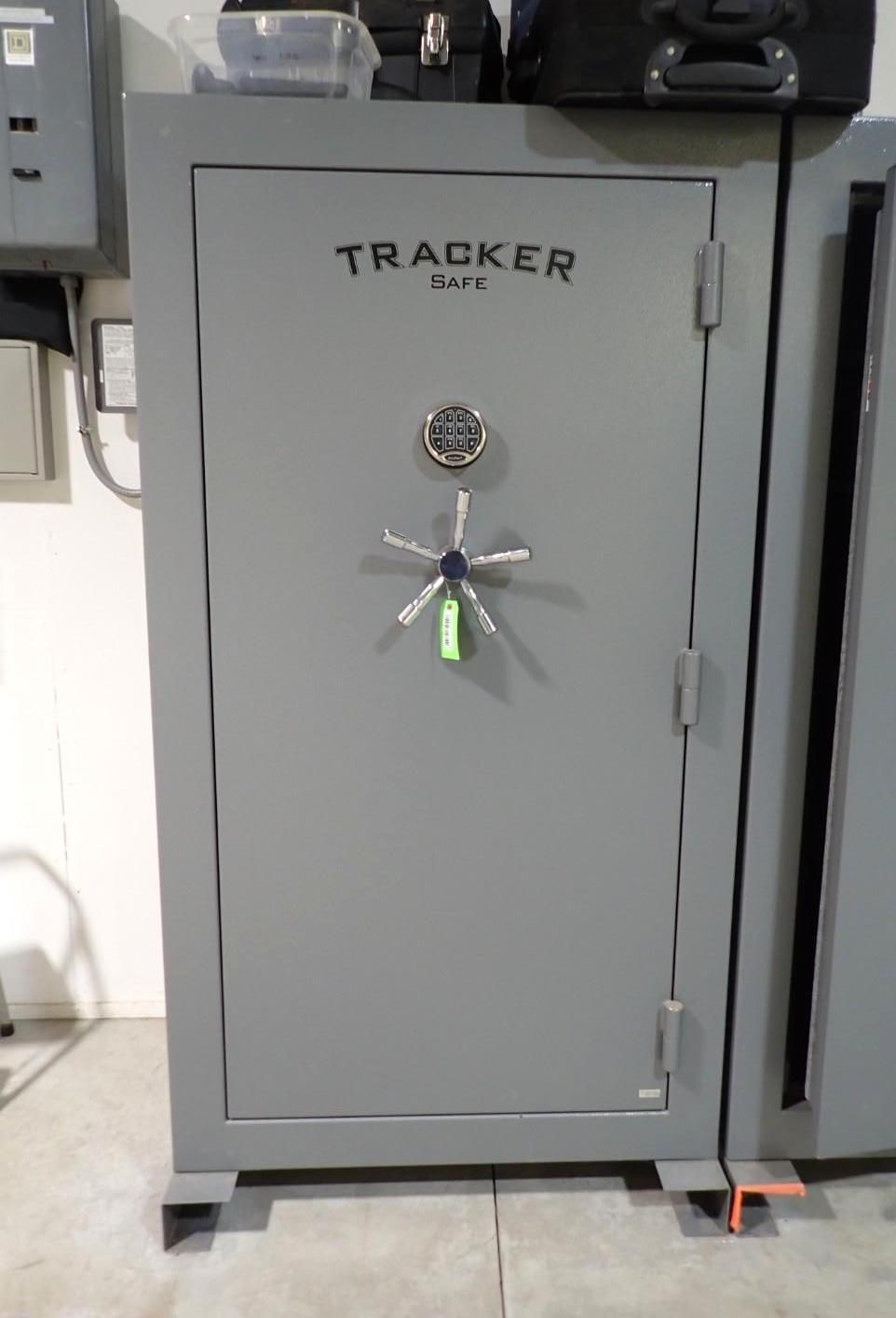 A gray Tracker safe with a six-spoke handle and a circular electronic keypad, positioned in a room.