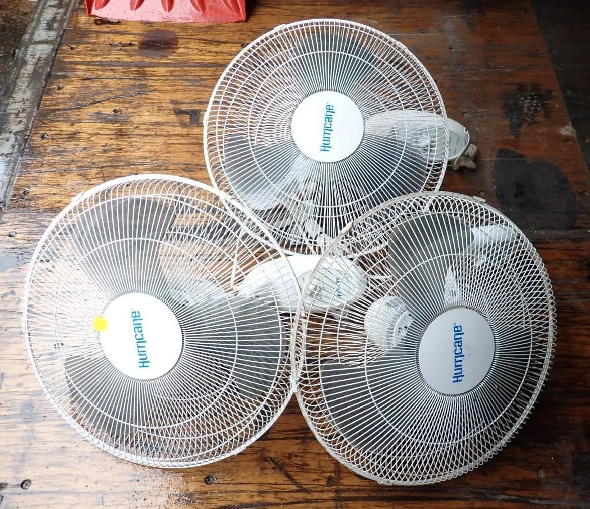 Three circular fan wire guards with brand logos displayed on a wooden surface.