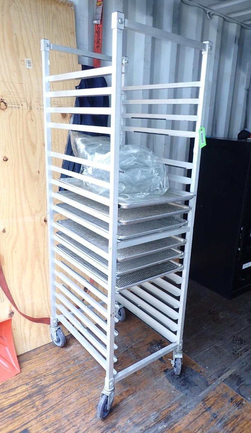 A metal bakery sheet pan rack with several trays stored inside, standing on wheels in a storage area.