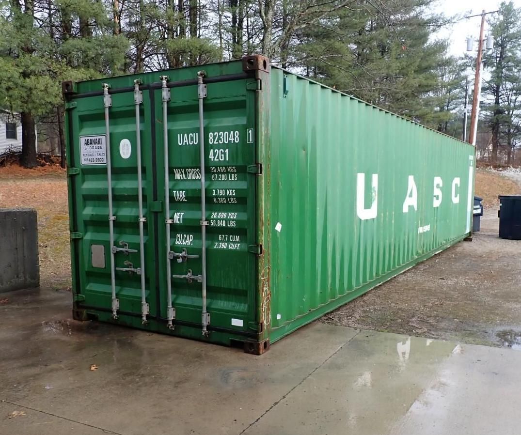 A green UASC shipping container sitting on a concrete pad in an outdoor, wooded area.