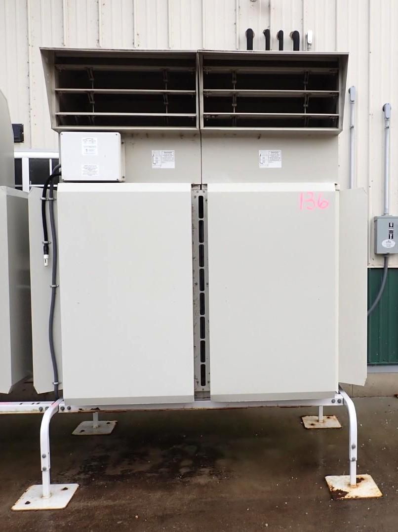 A light-gray commercial HVAC unit installed outdoors on metal legs against a white corrugated wall.