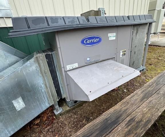 A gray Carrier HVAC unit with a large duct hood installed outdoors on a building's exterior wall.