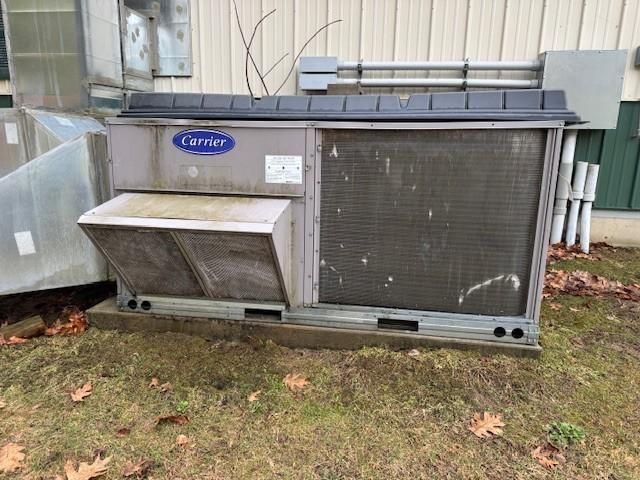A gray Carrier commercial HVAC unit sits outdoors on a grass patch beside a building wall.