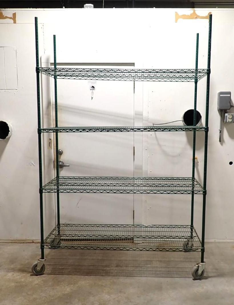 A tall, four-tiered industrial wire shelving unit with caster wheels, standing against a white wall.