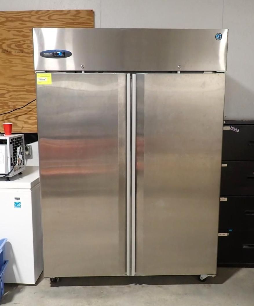 A stainless steel, two-door commercial refrigerator stands in a room with a small white freezer and black file cabinet.