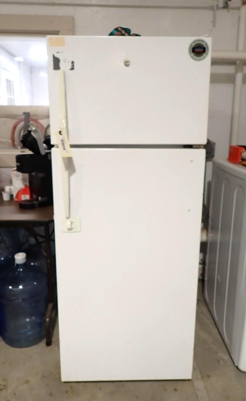 A white top-freezer refrigerator with a handle attached to the front, situated in a basement or garage setting.