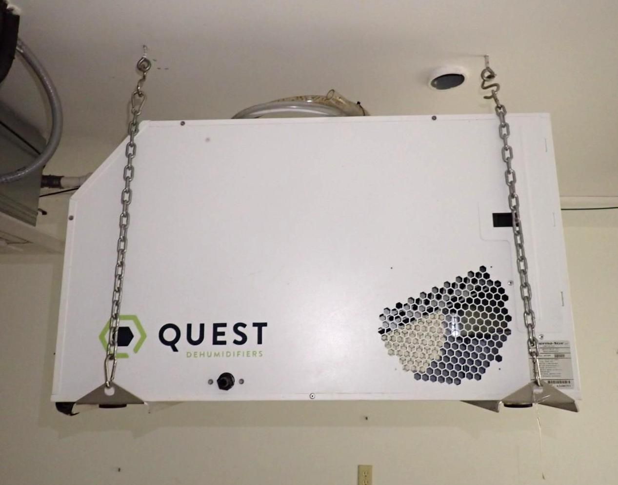 A Quest brand commercial dehumidifier suspended from a ceiling by metal chains.