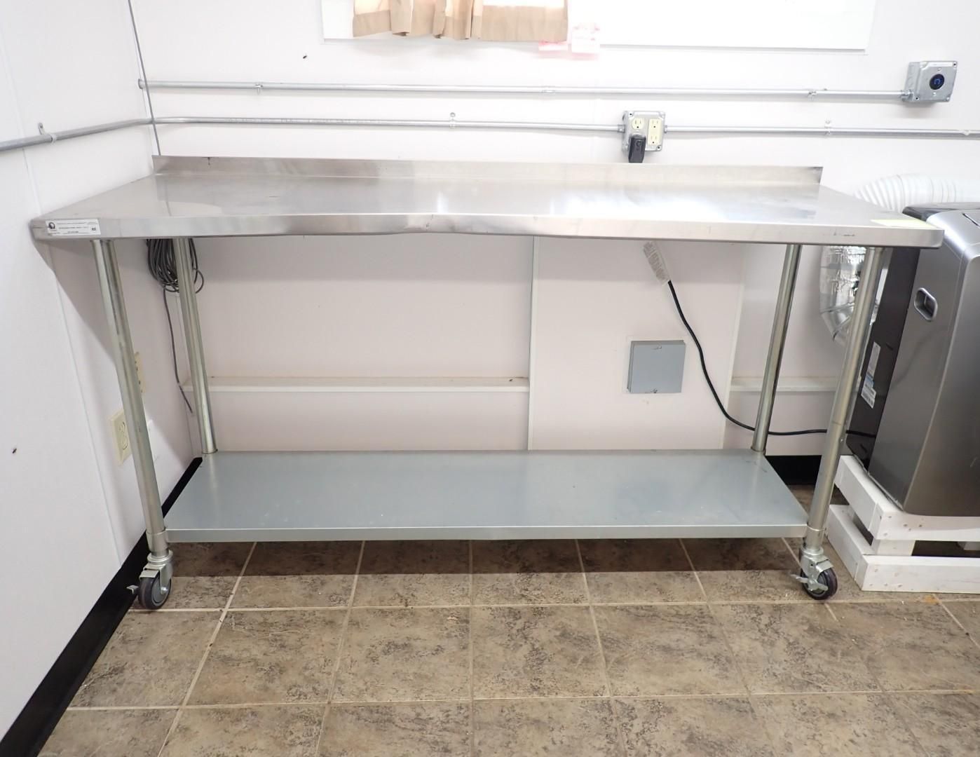 A stainless steel work table with a lower shelf, set on casters against a white wall with electrical outlets.