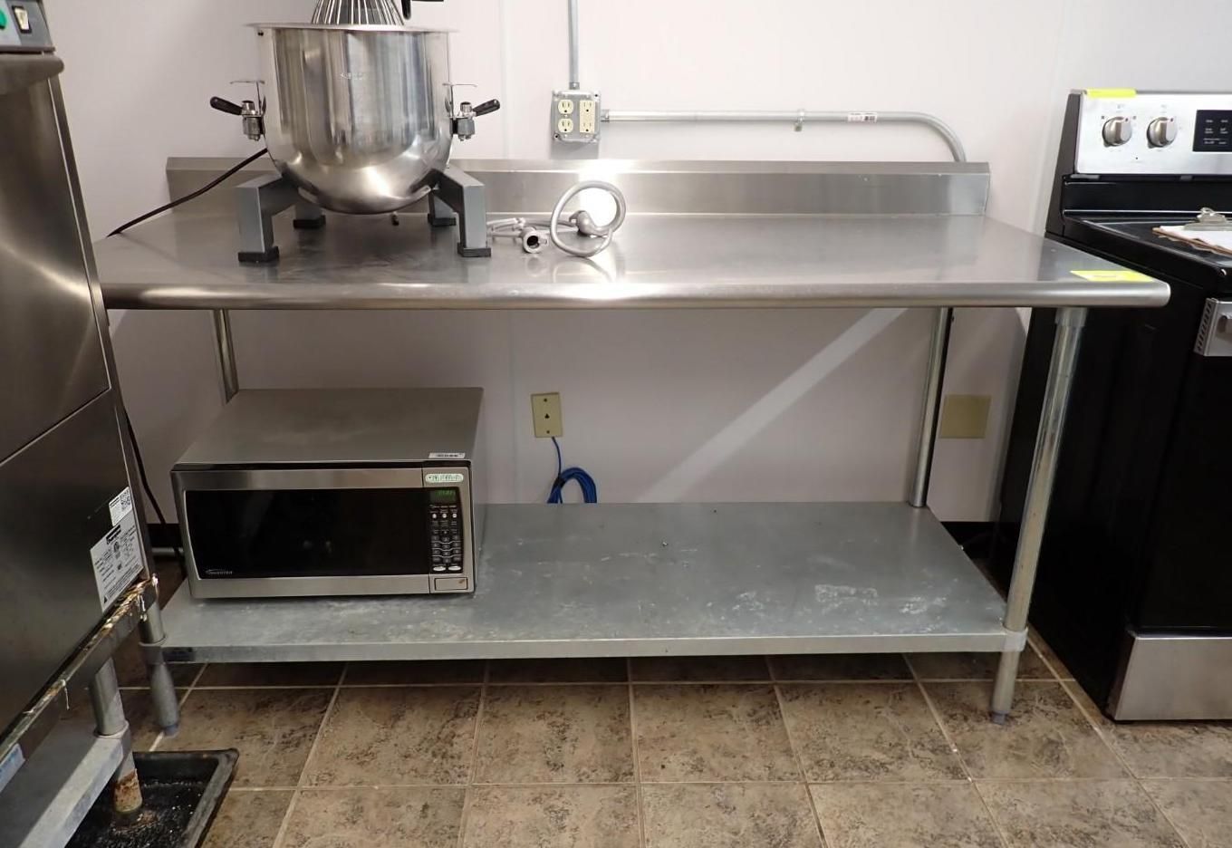 A stainless steel prep table with a commercial mixer on top and a microwave oven on the bottom shelf.