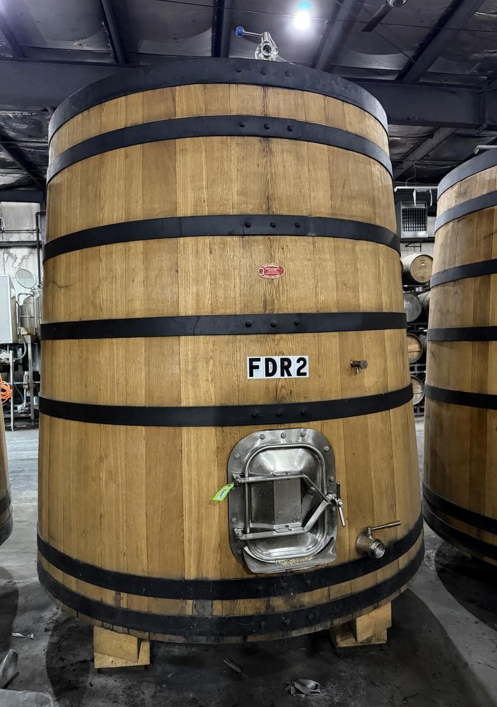 Large wooden barrel in a warehouse with black bands, labeled 