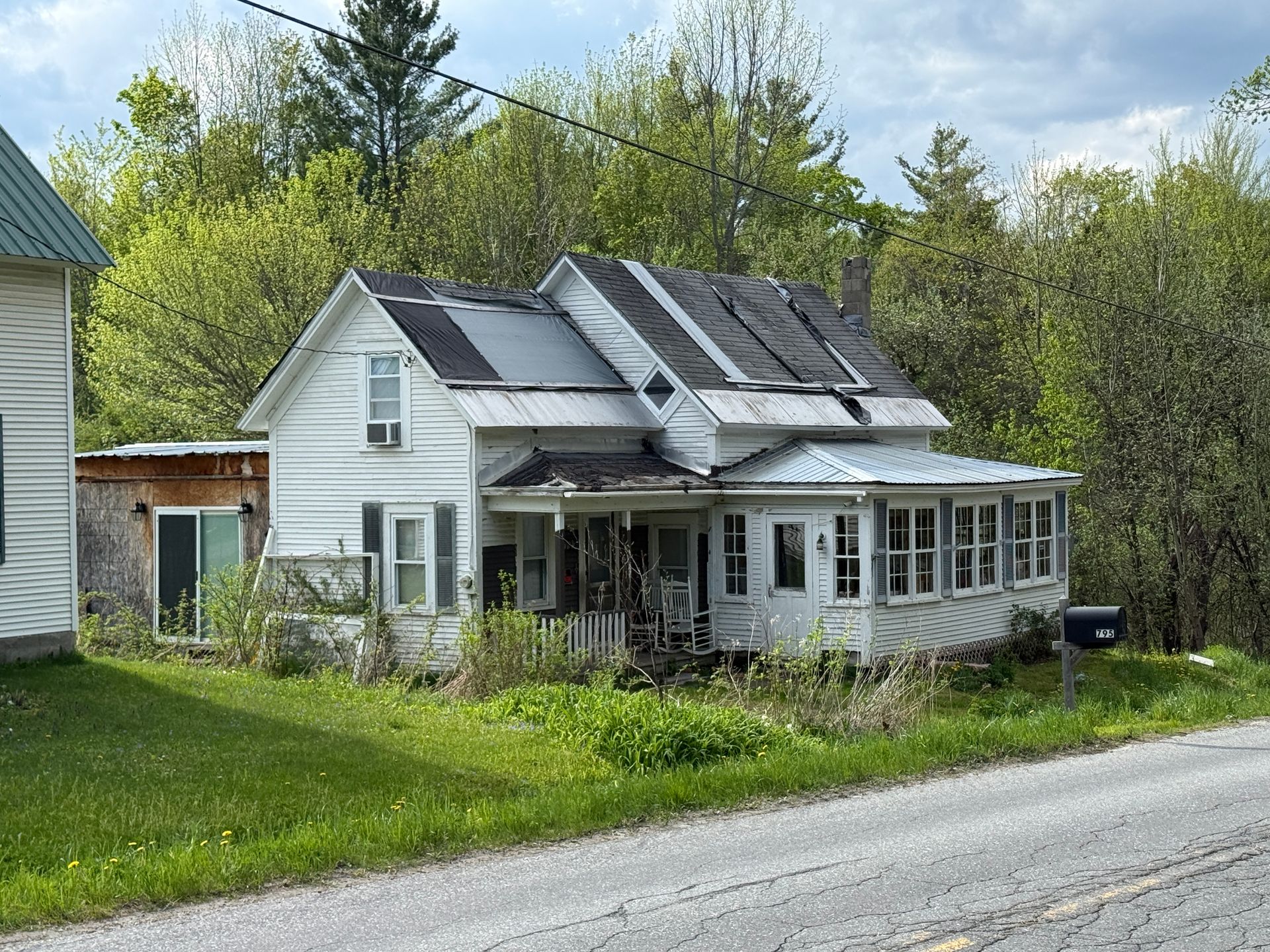 Old white farmhouse beside a gravel road, surrounded by trees and grass
