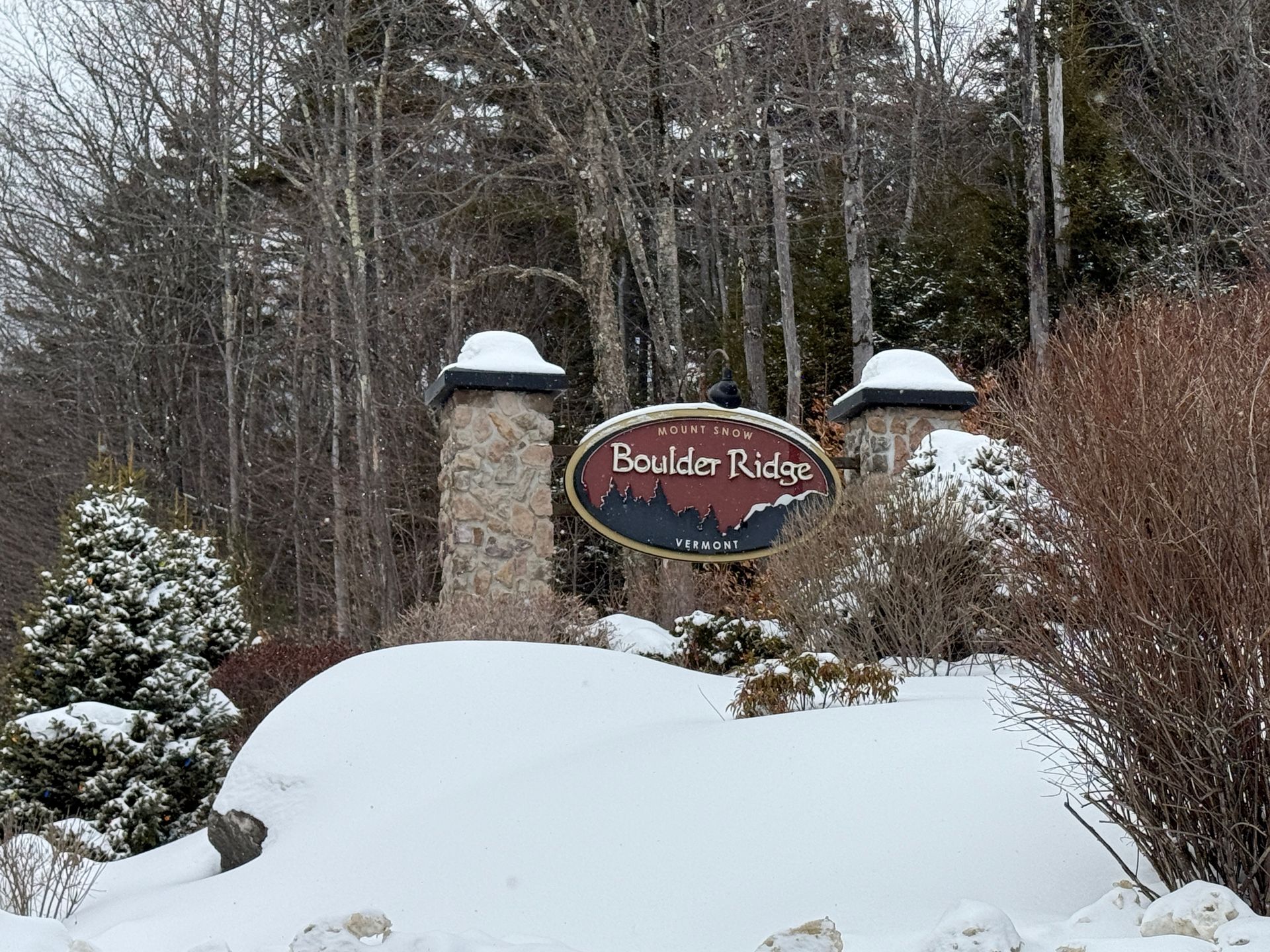 Sign for Boulder Ridge community in winter, flanked by stone pillars, trees, and snow. Foreclosure: Property.