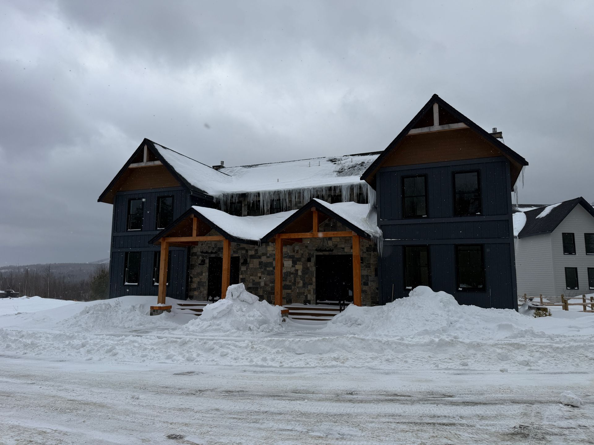 Snow-covered house under construction with dark siding and stone accents; Boulder Ridge Foreclosure Property.