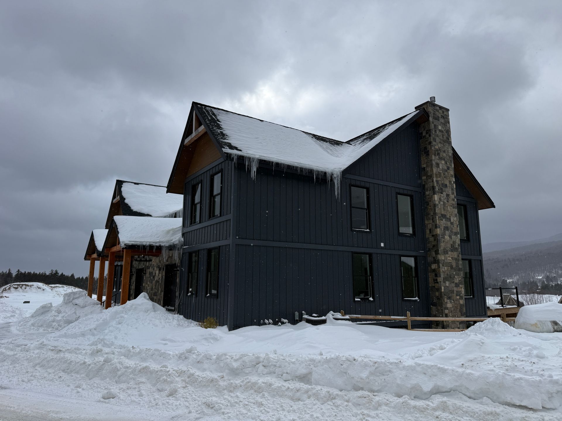 Two-story dark gray house with snow-covered roof, stone chimney, Boulder Ridge Foreclosure Property.