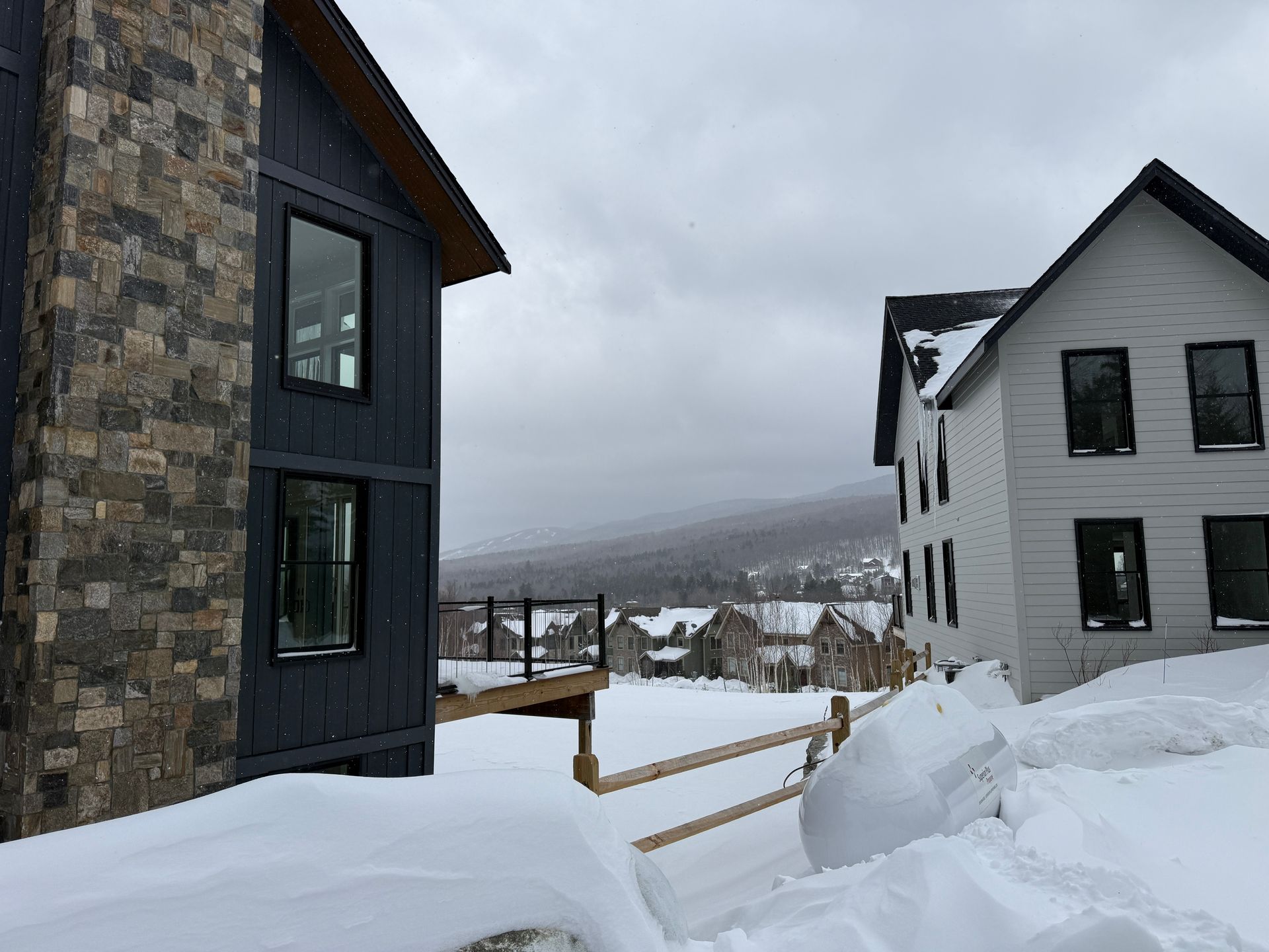 Snowy scene with two modern houses, one dark blue and one white, overlooking a valley. Boulder Ridge Foreclosure Property.