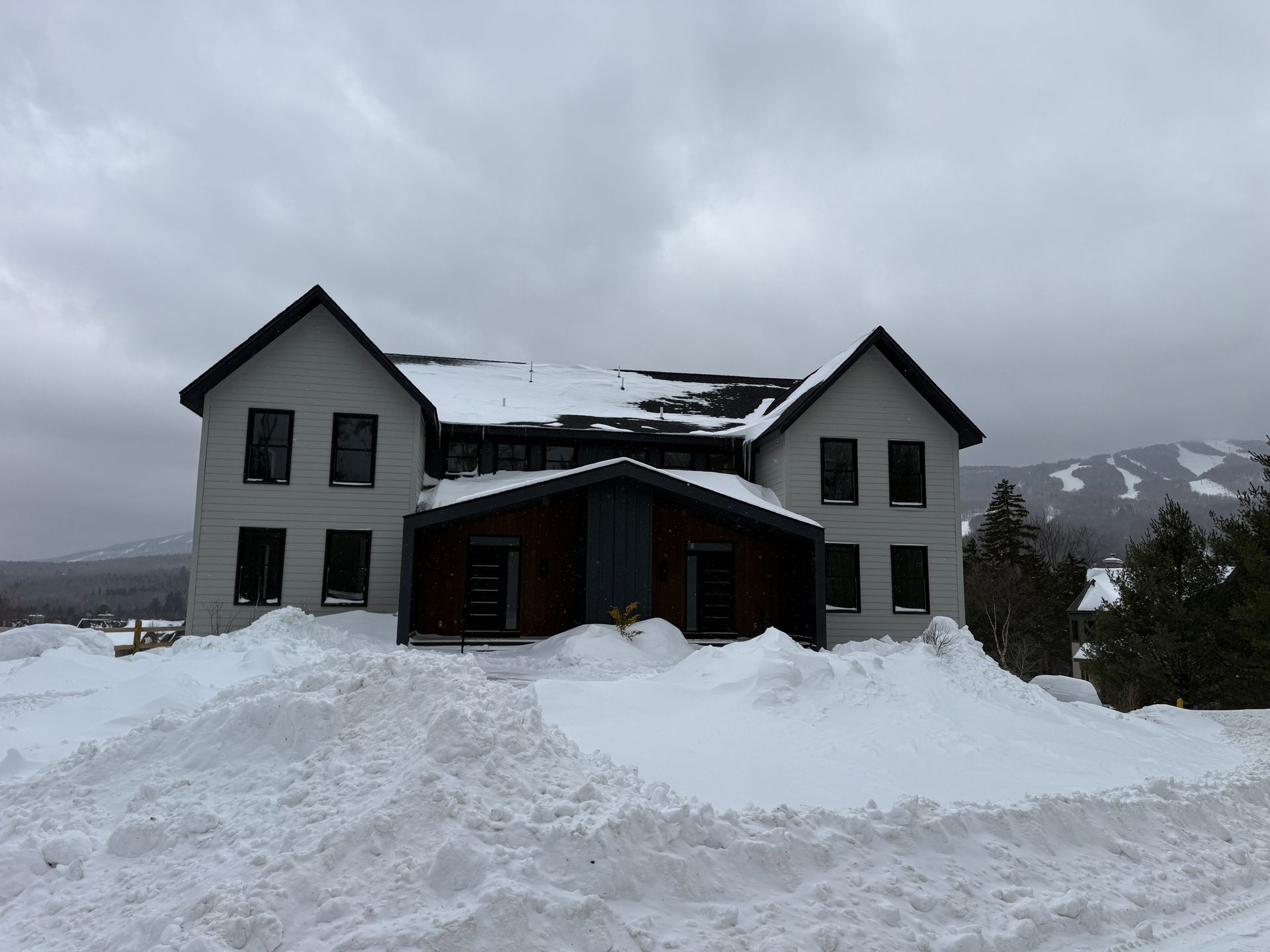 Two-story white building with black trim, surrounded by snowdrifts, under a gray sky. Boulder Ridge Foreclosure Property.
