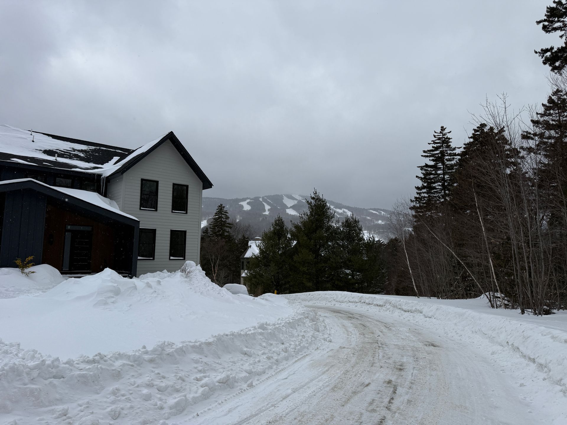 Snowy road in front of a gray building and ski slopes under a cloudy sky. Boulder Ridge Foreclosure Property.