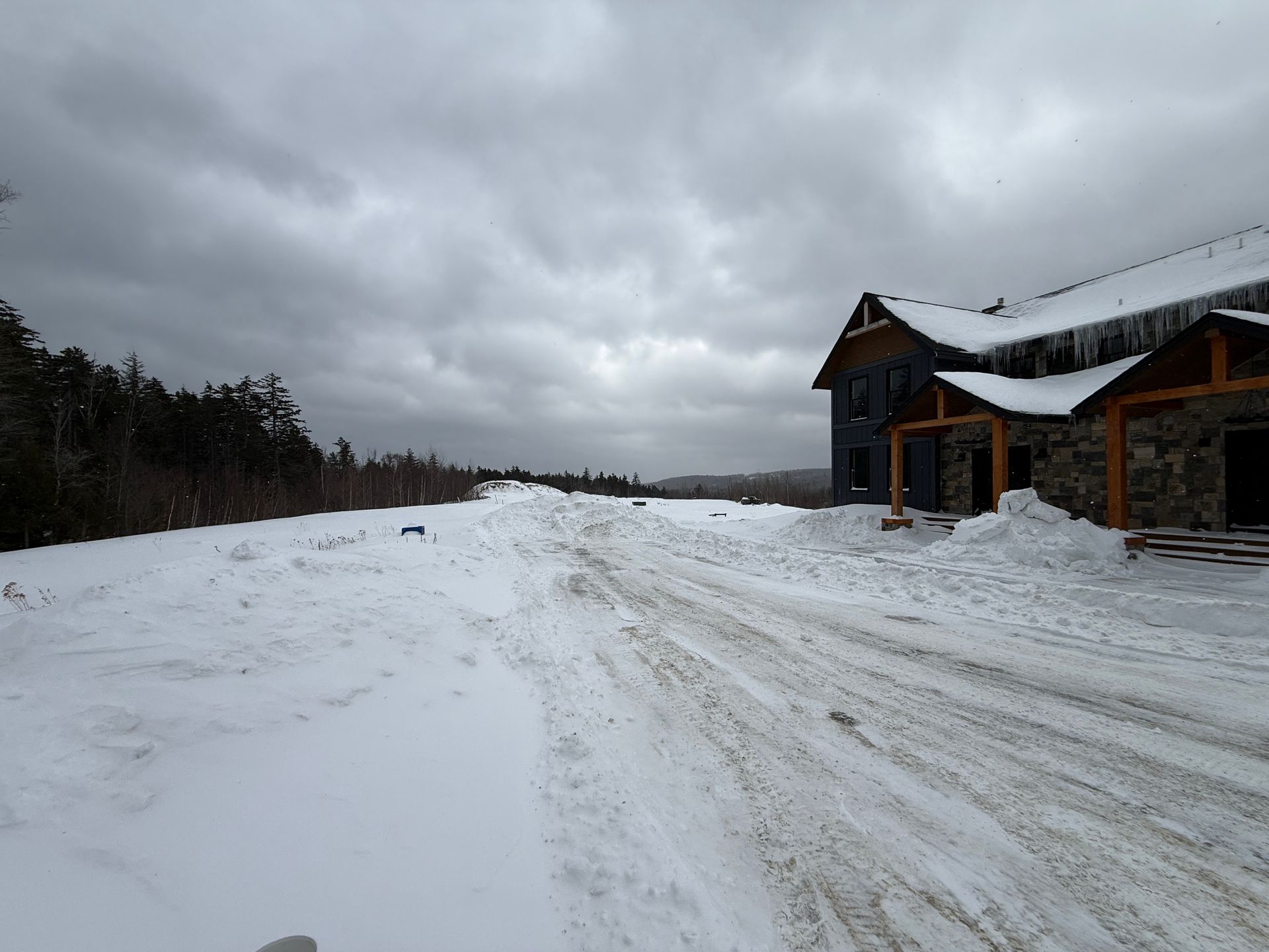 Snow-covered road leading towards a building with a dark facade, Boulder Ridge Foreclosure Property.
