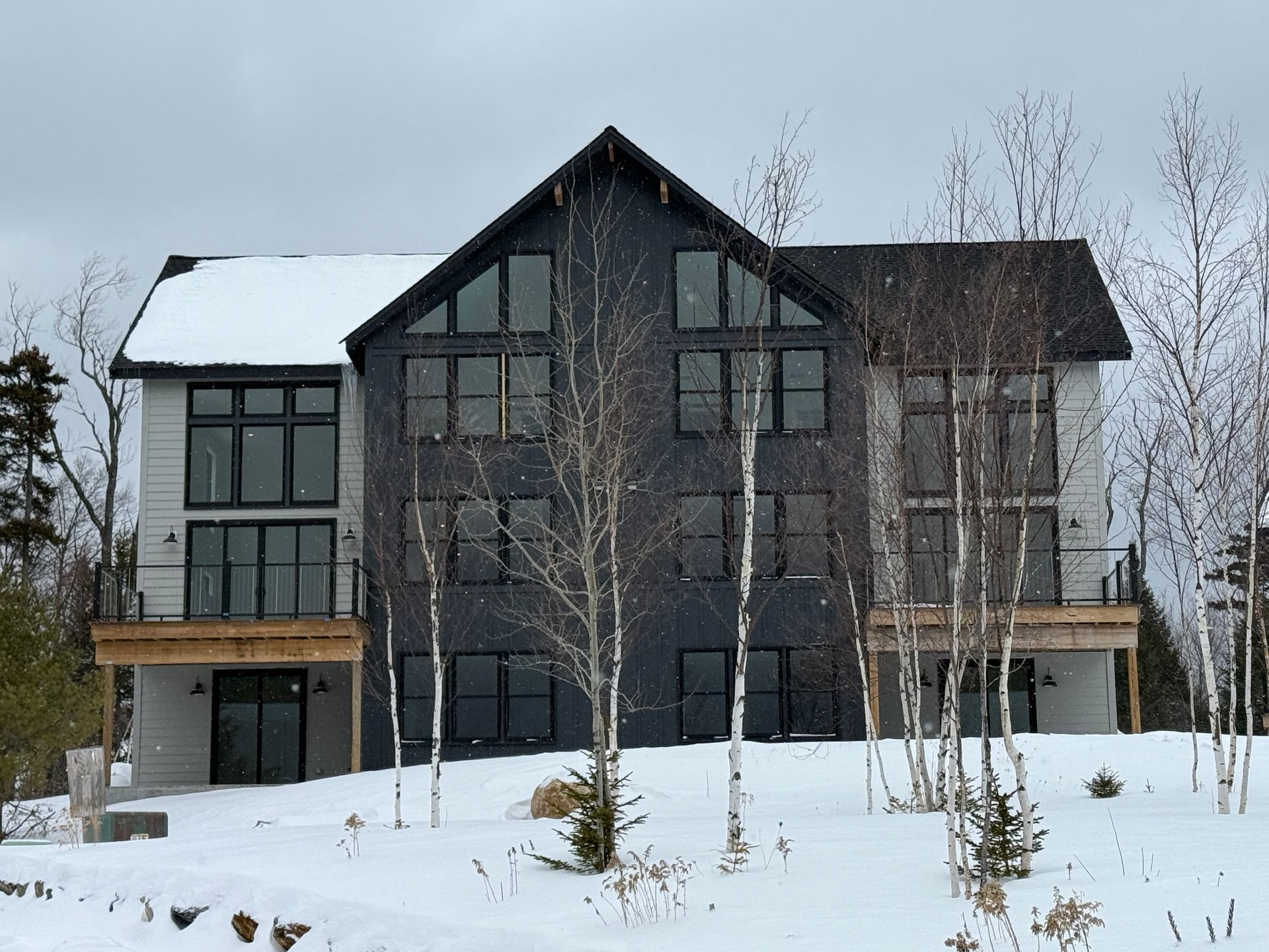 Modern two-story house with dark gray siding, large windows, snow-covered roof, and a winter landscape. Boulder Ridge