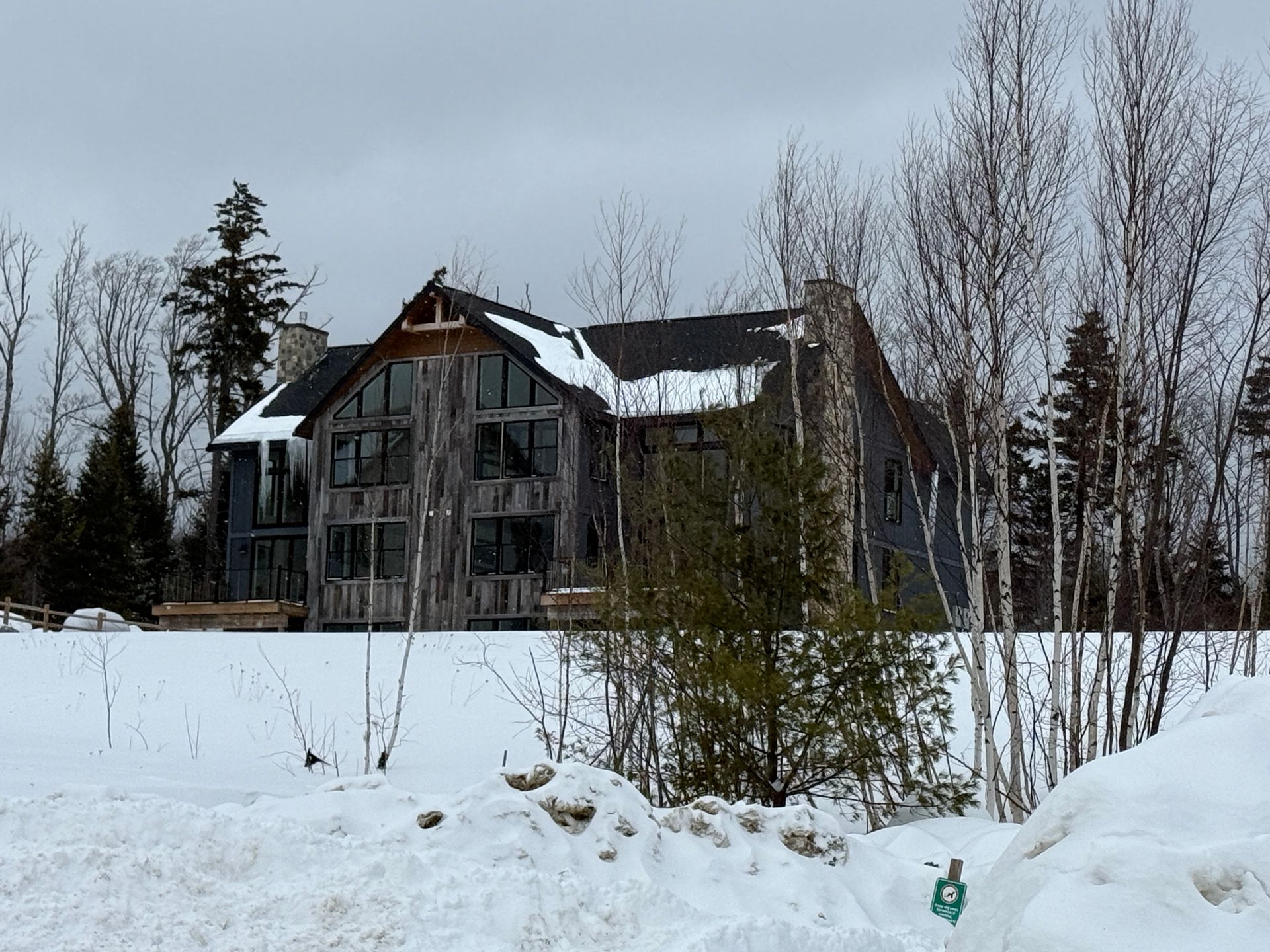 A large, weathered wooden house with tall windows in a snowy forest. Boulder Ridge Foreclosure Property.