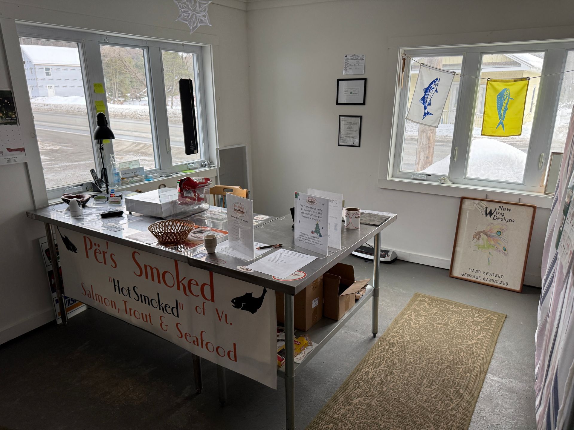 Small office with a desk, papers, wall art, and a window; a banner hangs on the front of the desk.