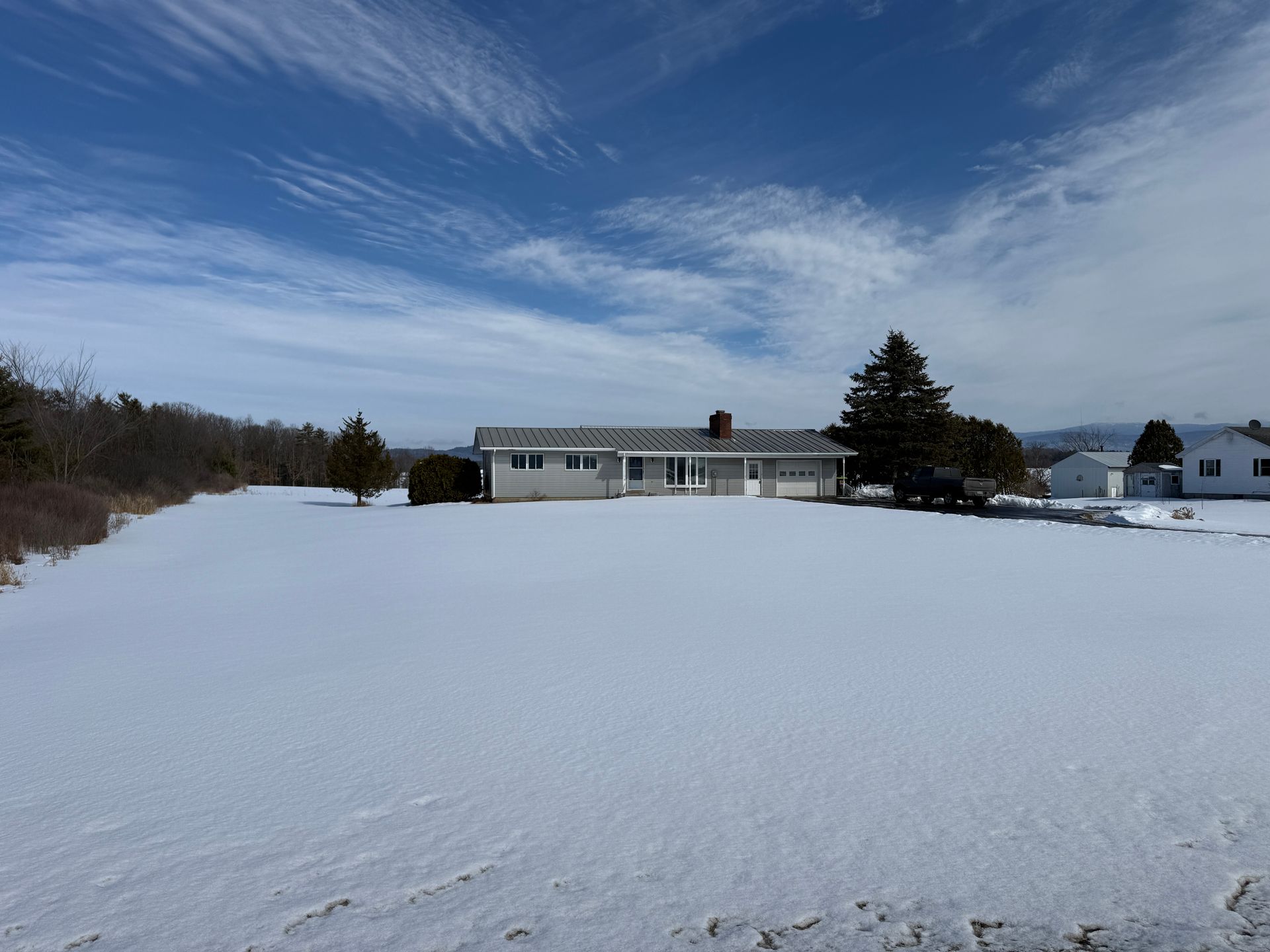 Snowy landscape with a single-story house under a blue, partly cloudy sky.