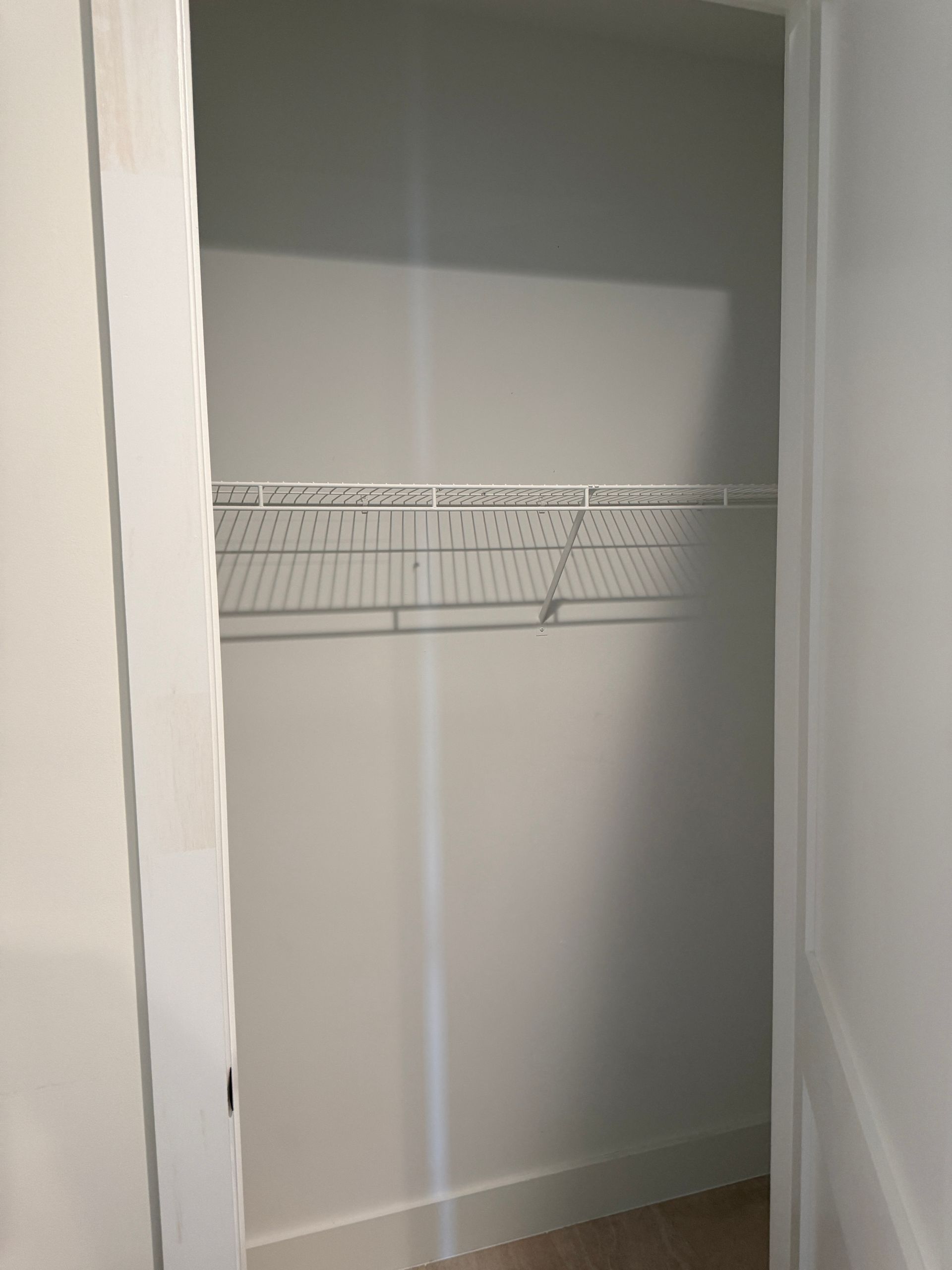 An empty walk-in closet with white walls and a single white wire shelf.