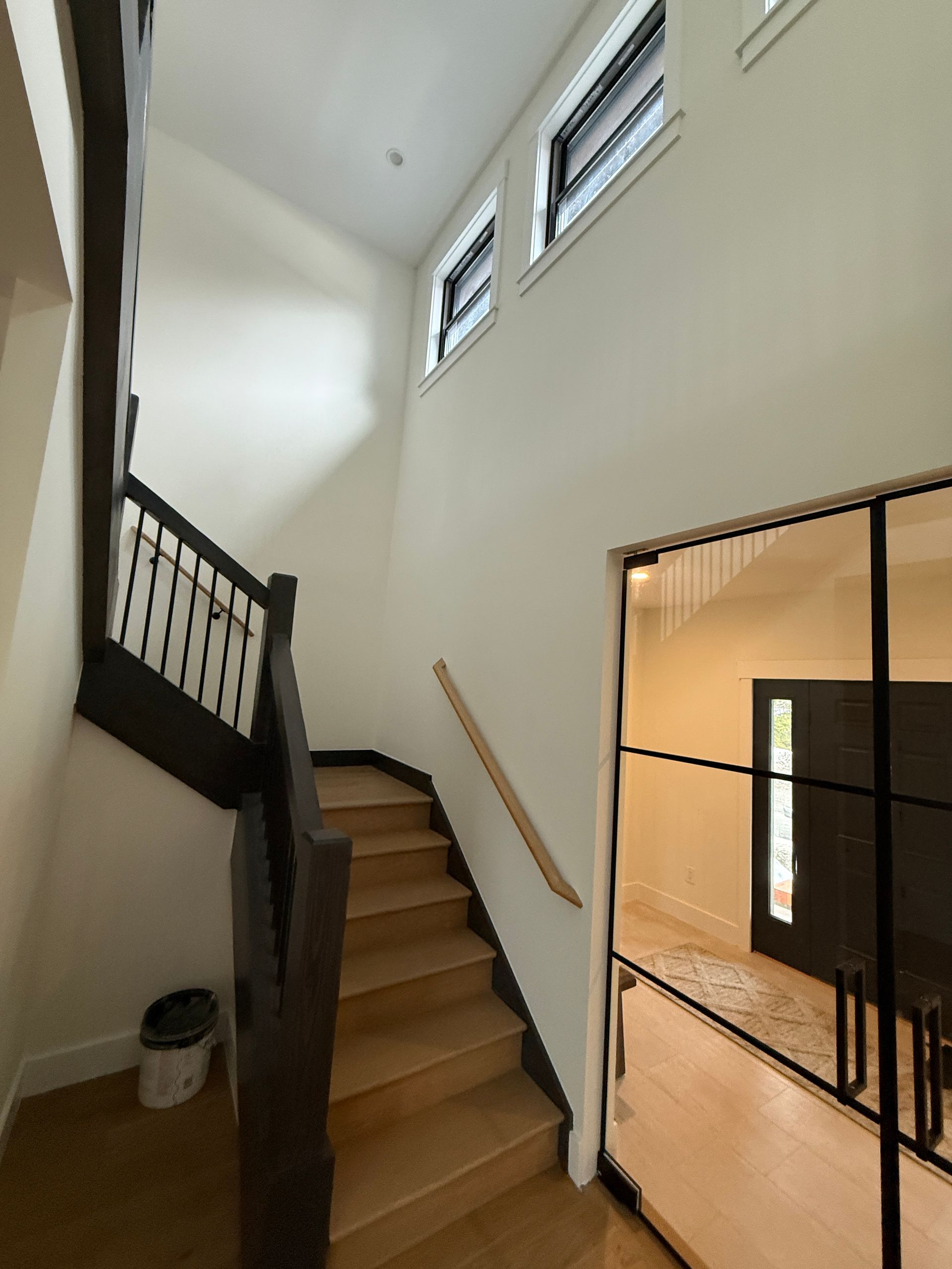 Staircase with light wood steps and dark railings next to a glass-paned door, set within a bright, modern interior.