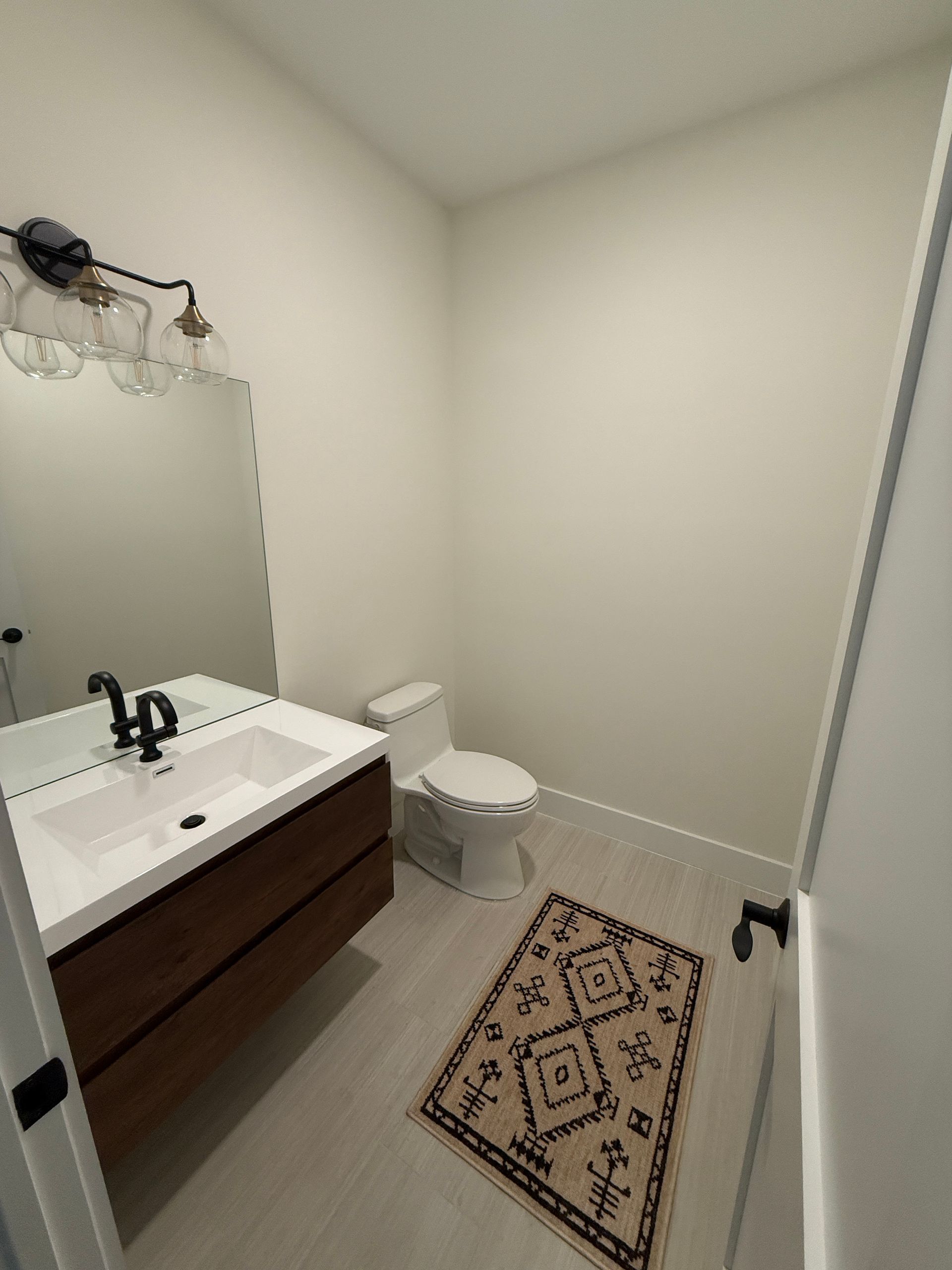 A modern bathroom featuring a floating dark wood vanity, a black faucet, a large rectangular mirror, and a geometric rug.