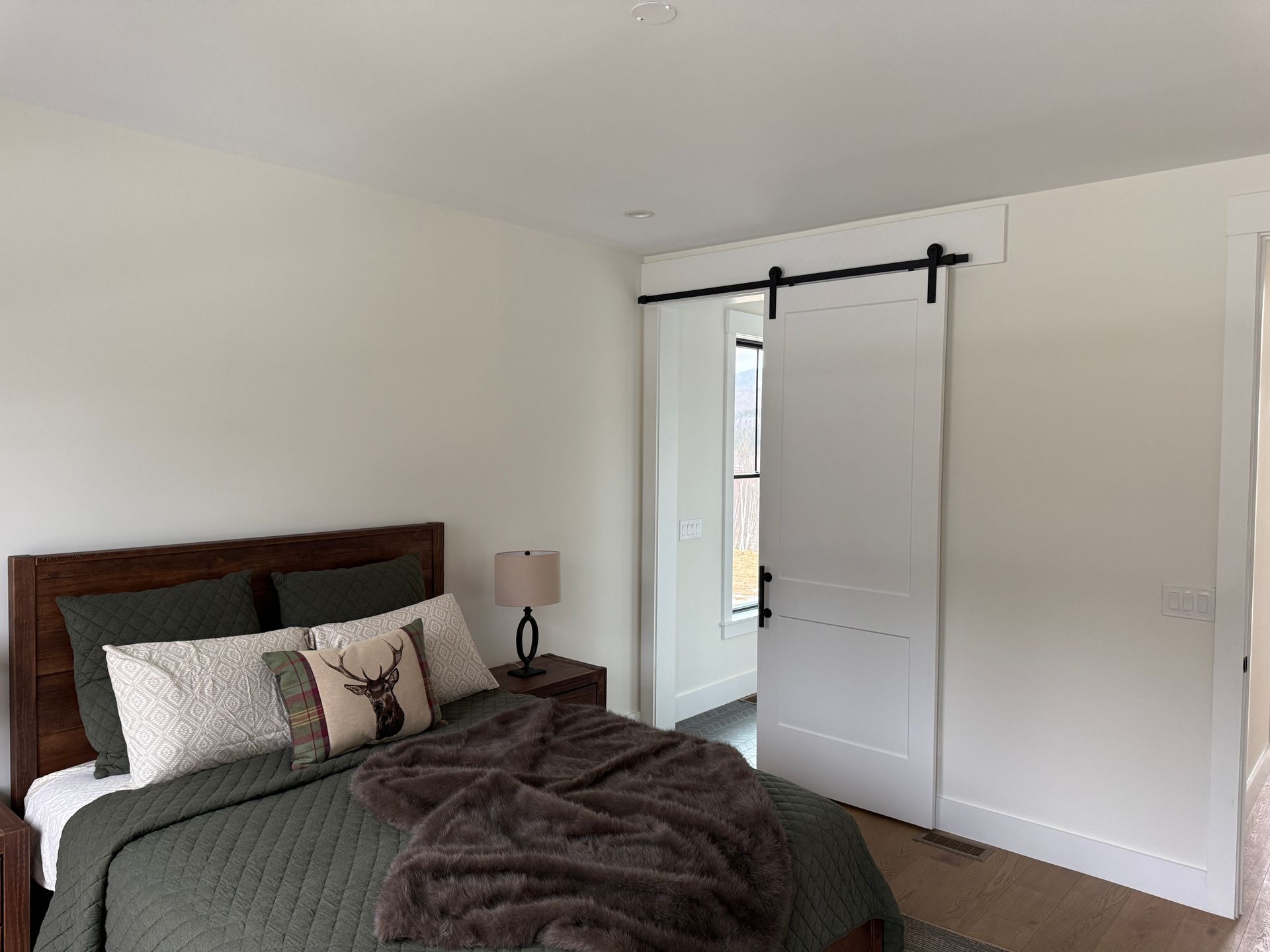 A modern bedroom with a dark wooden bed, forest green bedding, and a white sliding barn door on a black rail.